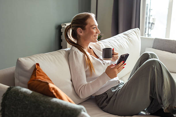 istock Young woman relaxing on couch while using smartphone and drinking coffee 2208272064