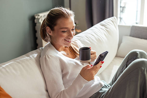 istock Young woman relaxing on couch while using smartphone and drinking coffee 2208272095