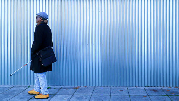 istock Blind mature man walking with his white cane next to a corrugated iron background 2208275876