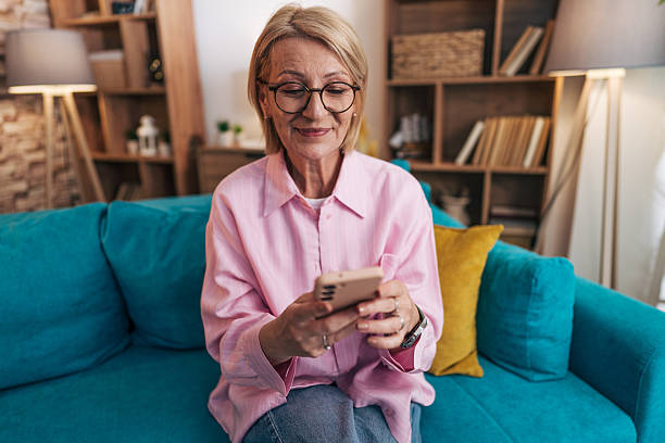 istock Smiling senior woman using smartphone on sofa at home 2208276998
