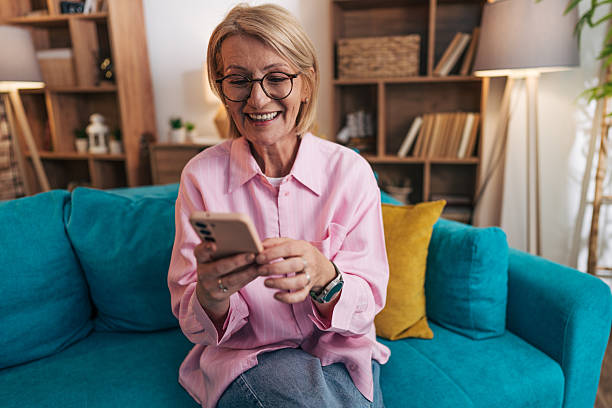 istock Smiling senior woman using smartphone on sofa at home: connecting with loved ones 2208277198