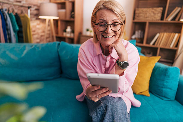 istock Smiling senior woman using digital tablet at home on sofa 2208277314