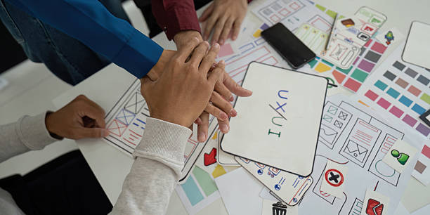 istock Collaboration and UX/UI Design. Team members unite hands over design concepts, emphasizing teamwork in the UX/UI design process. 2208277357