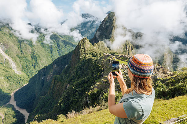 Traveler in colorful beanie photographing ancient ruins. Exploring iconic Machu Picchu landscapes. Enthusiast appreciating historical architecture and natural beauty.