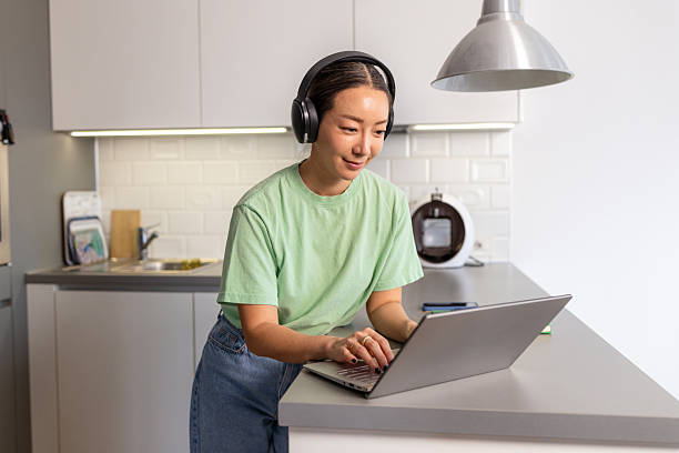 istock Woman with headphone in the kitchen, using a laptop 2208282456