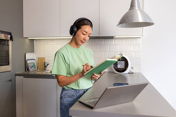 istock Woman with headphones at kitchen counter taking notes while working on laptop 2208282461