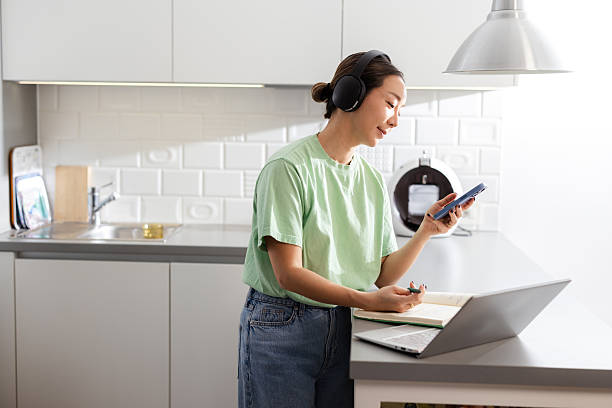 Woman working at kitchen counter multitasking with phone and laptop