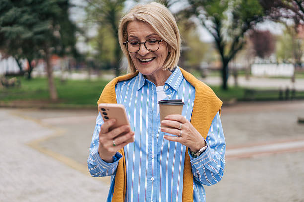 istock Smiling senior woman using smartphone and drinking coffee outdoors 2208283696
