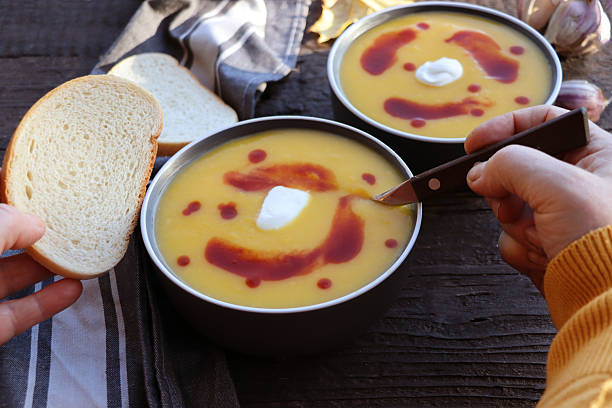 Female hands and Fall warming pumpkin cream soup  over rustic wooden table background, top view. Autumn vegetarian, vegan, healthy comfort food eating concept.
