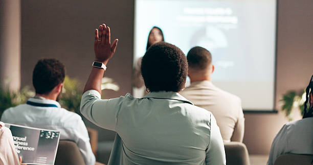 istock Business people, seminar and presentation with audience, question and interaction for feedback or engagement. Group, speaker and back of employee with hand raised for proposal or speech at convention 2208292067