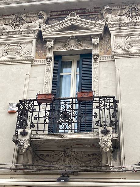 istock Wood shuttered window,  organic decorative wrought iron railing, lion headed brackets, garlands, relief columns floral motifs, cartouche, pediment with egg-and-dart, shell sculpture topping. 2208292499