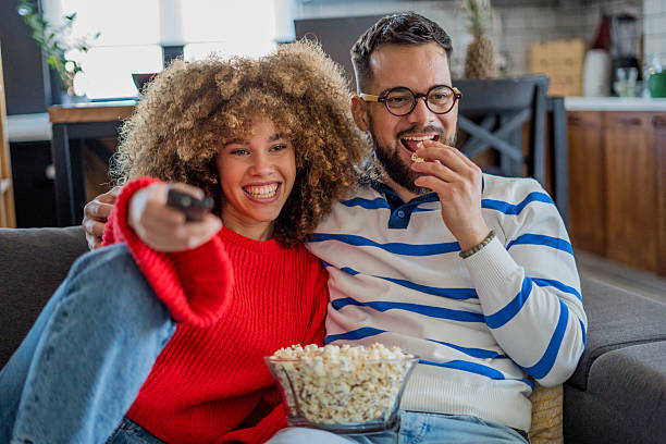 istock A young couple relaxes on a comfortable sofa, enjoying popcorn and laughing while watching a comedy on TV, happily spending time together at home 2208298159