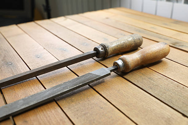 A close-up of vintage metal files with wooden handles on a rustic workbench. The focus is on the foreground file, highlighting its textured surface and worn grip, while the others fade into the background.