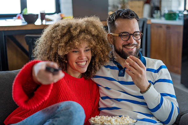 istock A young couple relaxes on a comfortable sofa, enjoying popcorn and laughing while watching a comedy on TV, happily spending time together at home 2208298896