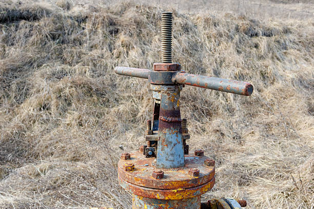 A weathered and rusty yellow gas pipeline valve stands in a dry grassy field, showing signs of aging, corrosion, and neglect.