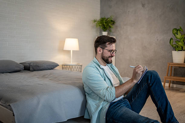 istock Young man sitting on bedroom floor and writing in notebook 2208312007