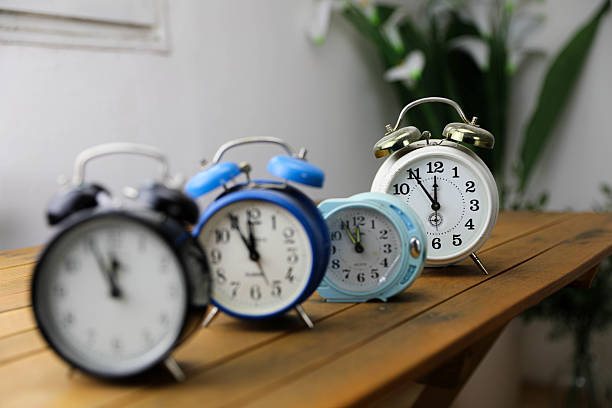 A collection of vintage alarm clocks displayed on a wooden board, showcasing their classic designs and aged patina. The warm tones of the wood contrast with the metallic details, evoking a nostalgic, timeless feel.