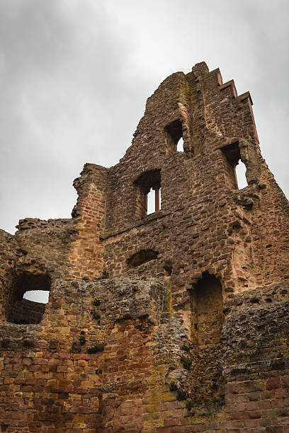 This striking structure showcases remnants of a medieval castle, with crumbling stone walls and arched windows. Overcast skies provide a dramatic backdrop to the historical site.
