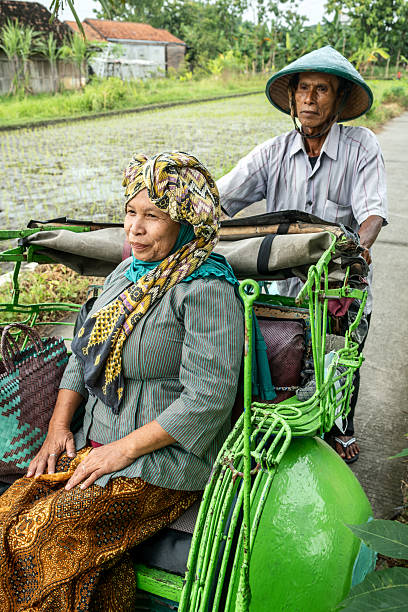 istock Elderly javanese woman riding in becak pulled by man 2208318204