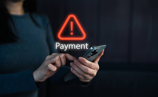 istock A person is using a smartphone, displaying a warning symbol related to payment issues in a dimly lit environment. 2208323914