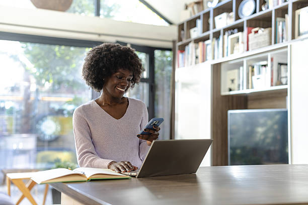 istock Smiling woman using a smartphone while working on a laptop at home 2208326174