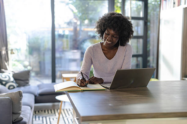 istock Young woman writing notes while working on her laptop at home 2208326213