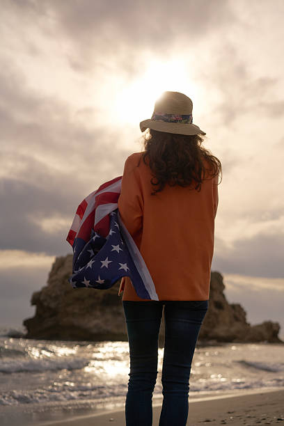 istock Woman Holding an American Flag on a Beach During a Dramatic Sunset While Exploring Nature's Beauty 2208328814