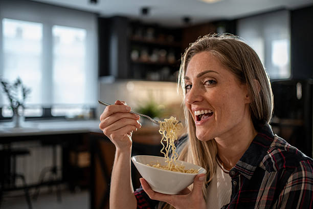 istock Happy woman enjoying noodles in her modern kitchen 2208335730