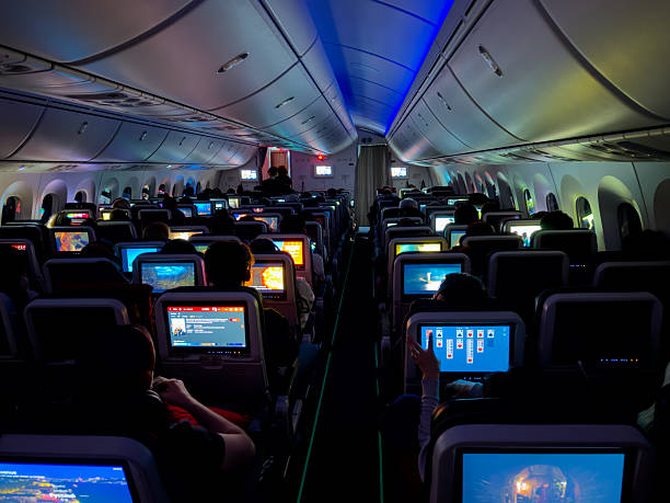 ISTANBUL AIRPORT, TURKEY, 30th JANUARY 2024: CLOSE UP: Tourists aboard a commercial airplane use their in-flight entertainment screens to watch flight details, movies and play games in the dark.