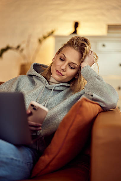Young Woman Relaxing at Home Using Laptop and Smartphone on Couch