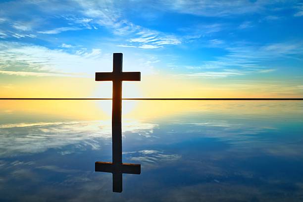 Dark cross on a reflective sand beach, as the sun setting on the horizon.