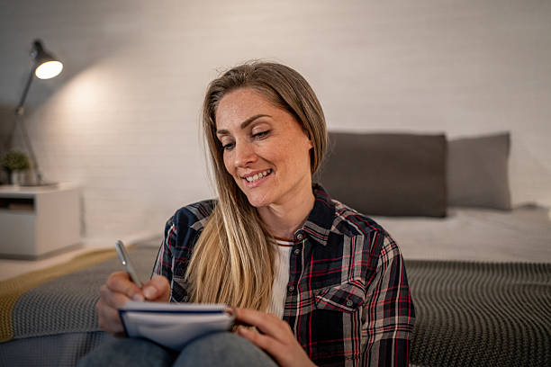 istock Smiling woman writing on notepad in bedroom at night 2208346294