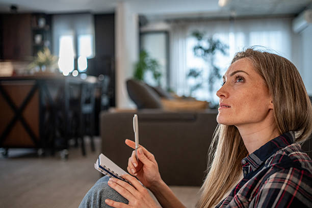 Woman sitting on floor holding pen and notebook, thinking