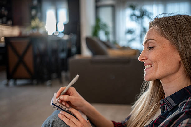istock Young woman taking notes in notepad at home smiling 2208346320