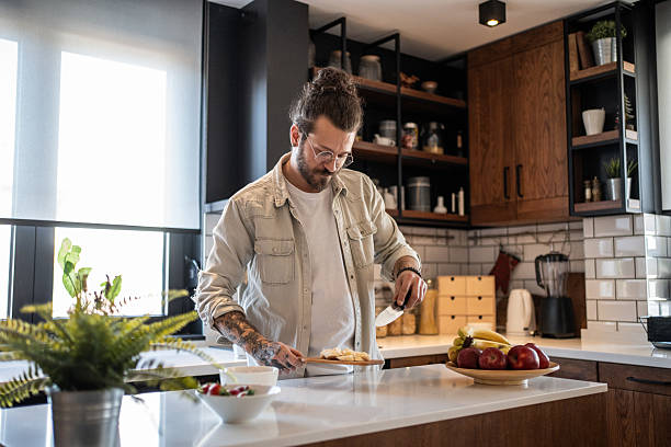istock Young man slicing banana on cutting board in modern kitchen 2208349265