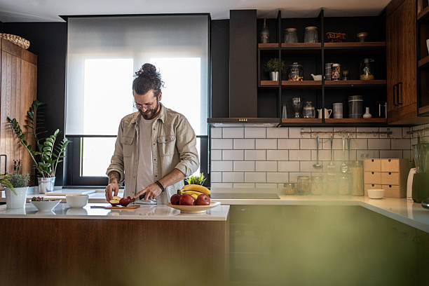 istock Young man cutting apples in a modern kitchen 2208349348