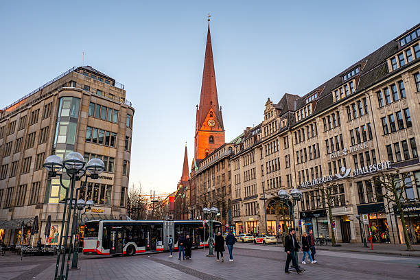 Hamburg, Germany. March 31st, 2025: The beautiful St. Peter's Church in Hamburg, with its tall red brick spire glowing under the warm light of the setting sun. The surrounding architecture combines modern and historic styles, while the spacious pedestrian area remains peaceful, emphasizing the serene and majestic atmosphere of the scene.