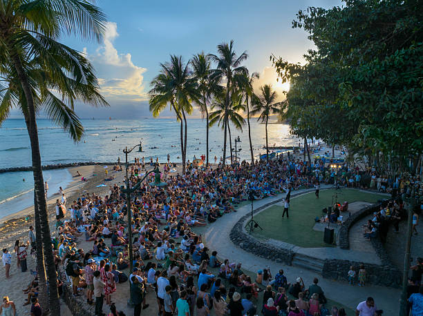 Hawaii  United States June30, 2024:This vibrant photograph captures the lively atmosphere of Waikiki Beach in Honolulu during sunset. The image showcases a large crowd gathered along the shoreline, enjoying the stunning sunset and the beach's festive ambiance. The golden light bathes the scene, highlighting the palm trees, the ocean's gentle waves, and the silhouettes of people enjoying the evening.