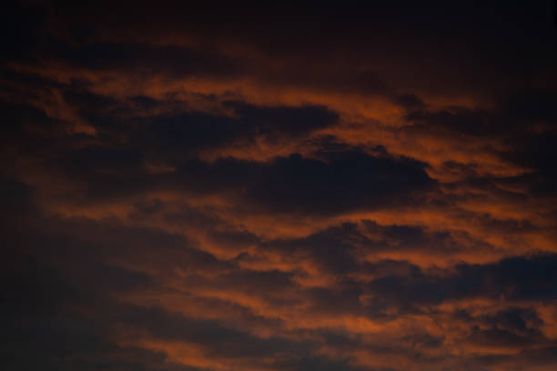 Dramatic clouds fill the sky at twilight, showcasing a beautiful blend of dark and vibrant orange shades. This natural spectacle creates a captivating backdrop for the evening.
