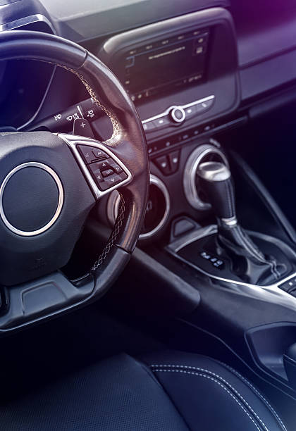 Car interior showcasing sleek steering wheel with control buttons, gear shift at center console, and touchscreen dashboard, captured daytime, no people, ideal for automotive design and tech themes.