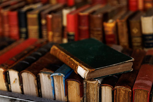 A stack of books with a green book on top. The books are old and worn