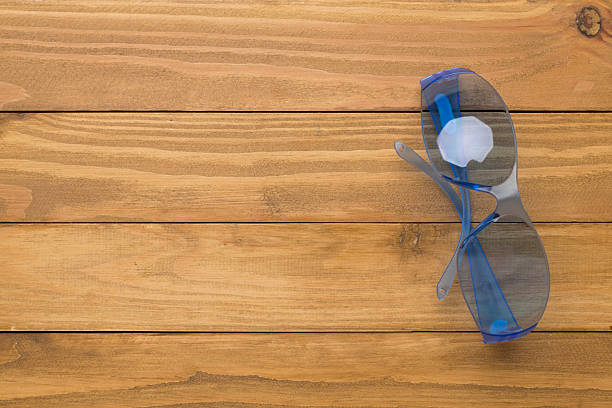 Safety glasses on wooden background, top view