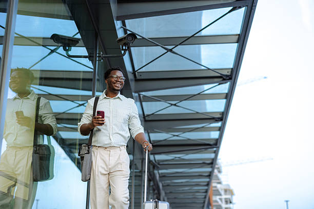 istock Confident man traveling with a suitcase and phone outside a modern building 2208374482