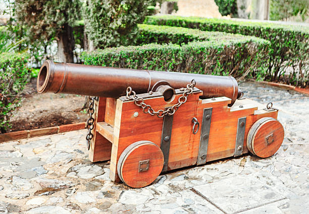 Historic iron cannon on a sturdy wooden carriage, maritime and fortress defense. Set on a stone pathway with lush greenery, it adds an authentic touch to historical and military-themed collections