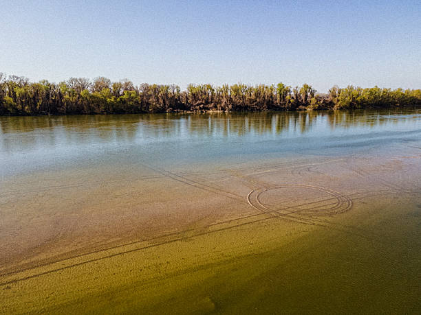 Nature, forests, sandy riverbed & transparent calm Danube river waters with sun reflections, viewed from above. Earth view for nature concepts & backgrounds.