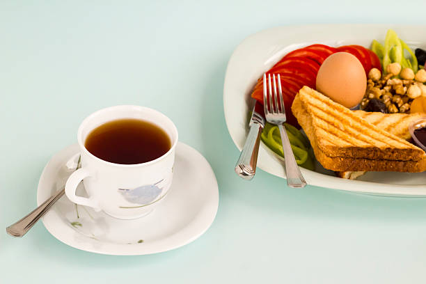 Breakfast plate with cheese toast and boiled egg and sliced tomato and a cup of tea