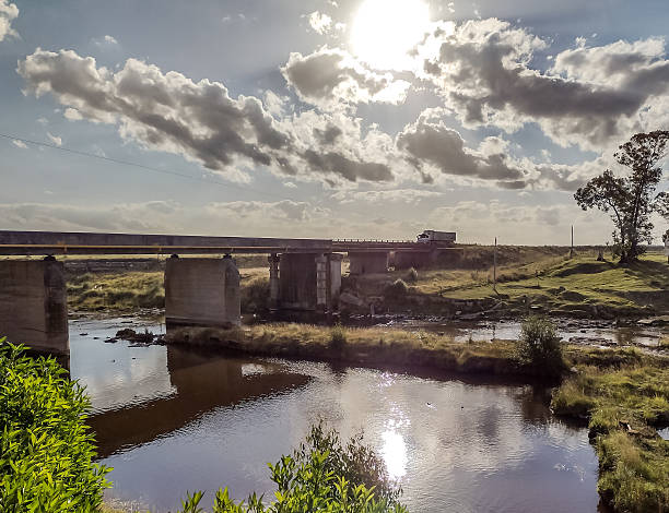 Truck crossing a bridge over a stream with the sun behind the clouds.