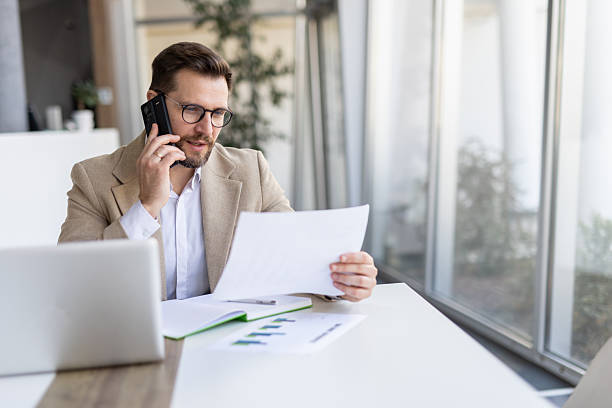 istock Man on phone reviewing papers in bright office space 2208402339