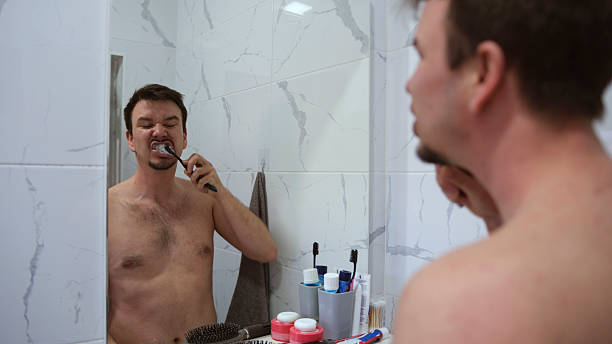 istock A sleepy student diligently brushes his teeth in front of a mirror. The mirror reflects the man's face and the countertop in the bathroom 2208408185