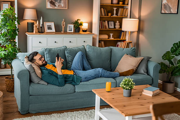 Happy young man relaxing on sofa and using smart phone at home.